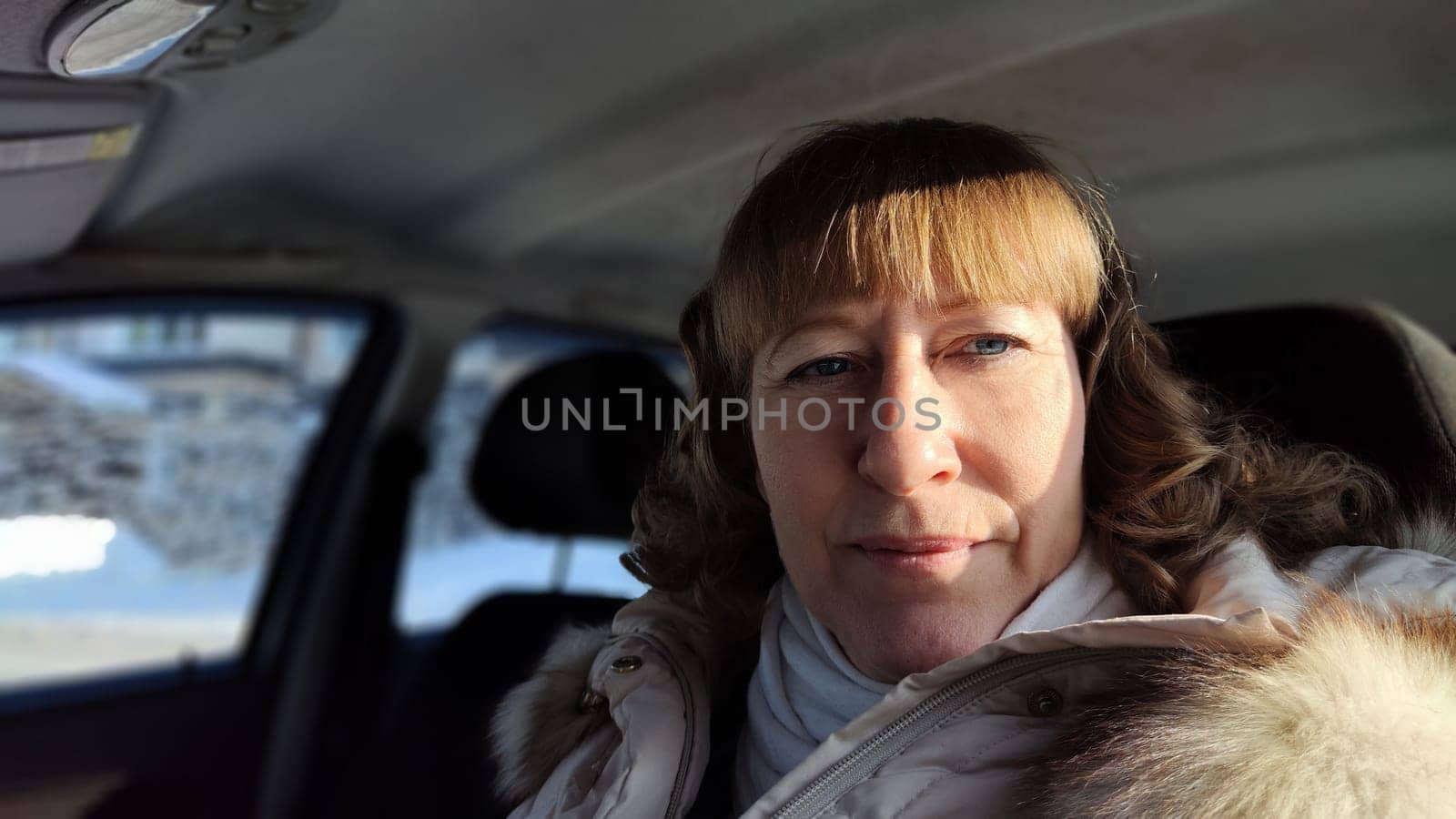 Woman sitting in the car in road trip. Blonde senior Woman driving transport. Lady travelling in cold time