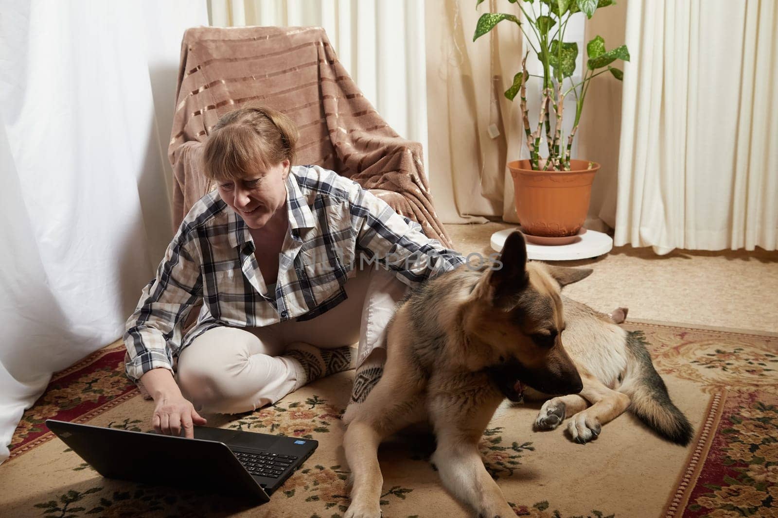 Woman and shepherd dog with netbook in living room. Portrait of a pet and a girl with laptop having fun and joy. Partial focus