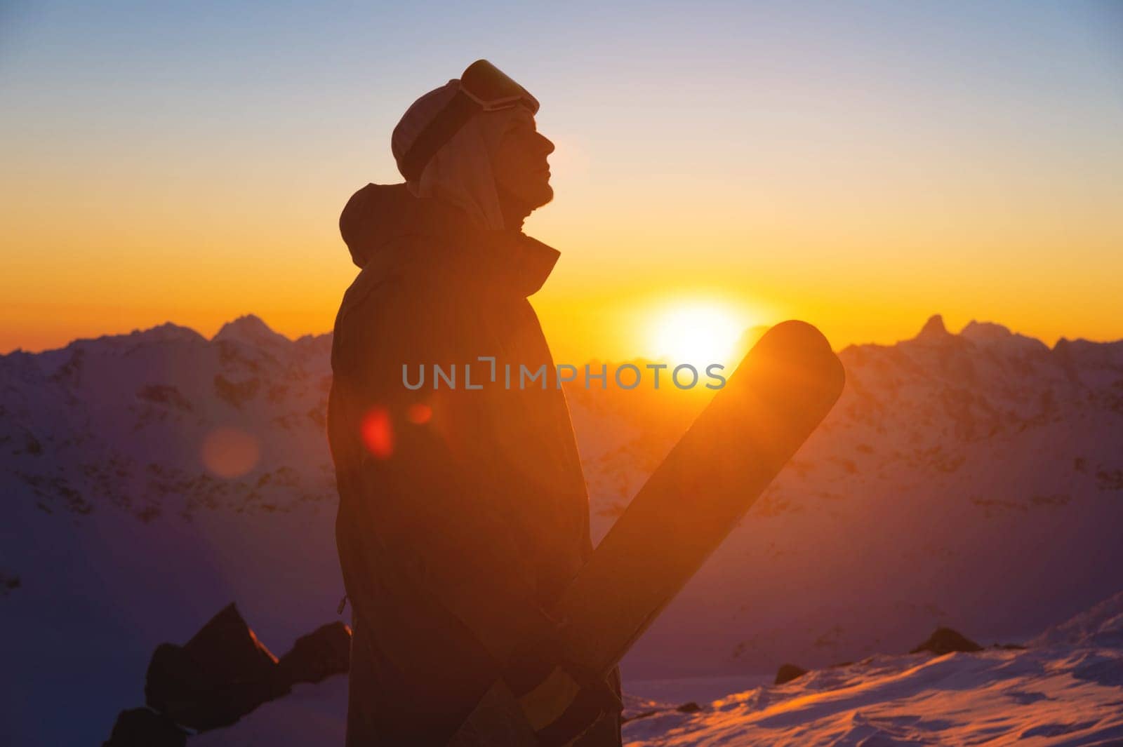 silhouette of a skier with skis standing on a slope at sunset against a mountain range. sportsman portrait by yanik88