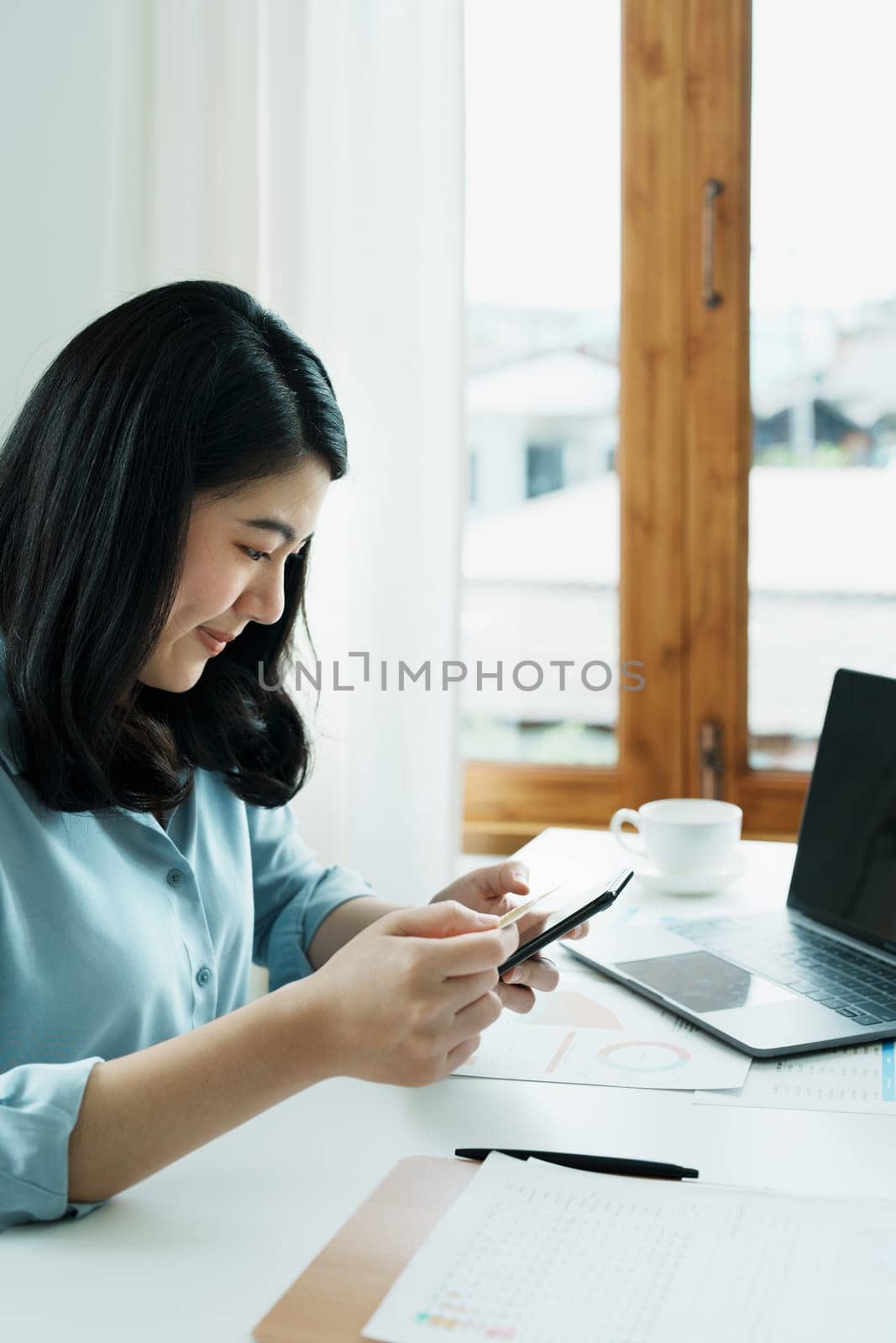 Portrait of young Asian woman using credit card and phone for online shopping by Manastrong