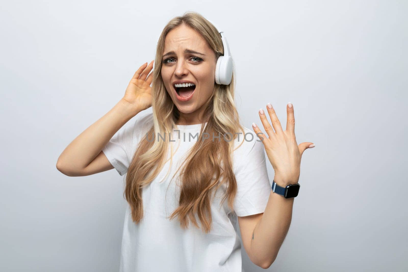 young woman sings along to music from headphones among white background.