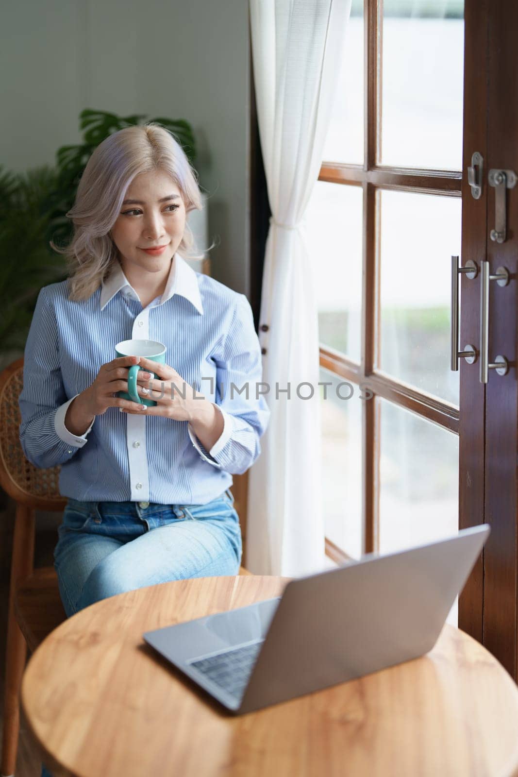 Portrait of an Asian business woman drinking coffee while working with a computer on her desk.