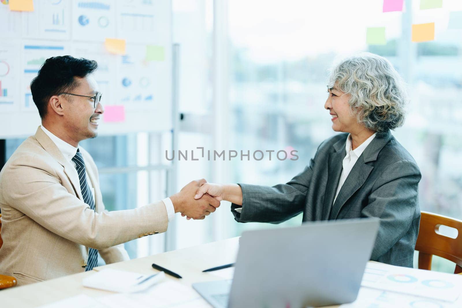 Asian entrepreneurs handshakes to congratulate the agreement between the two companies to enhance investment and financial strength. deal concept by Manastrong