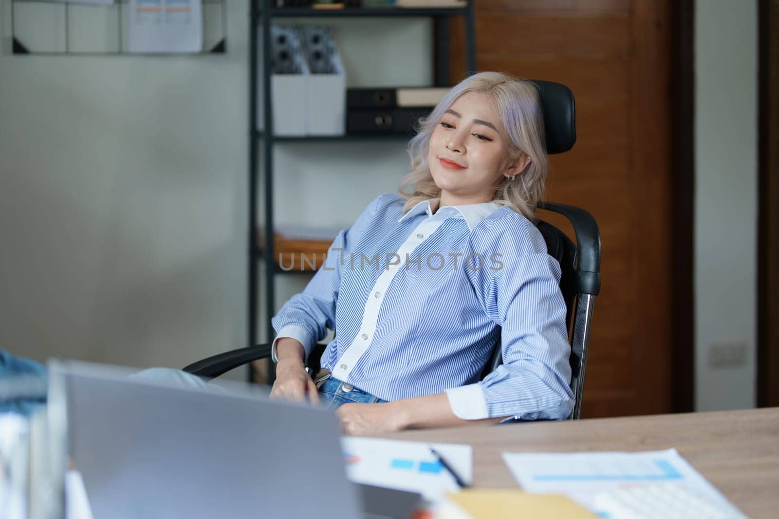 Portrait of a woman business owner showing a happy smiling face as he has successfully invested her business using computers and financial budget documents at work.