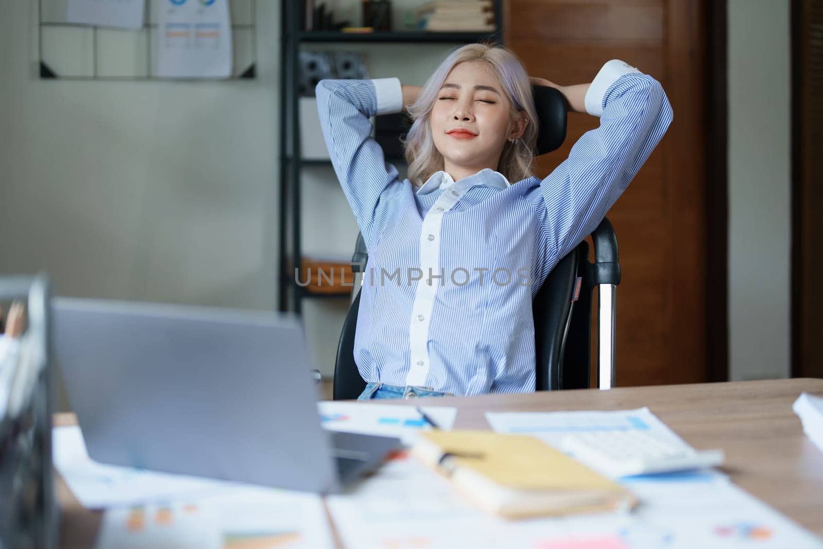 Portrait of a woman business owner showing a happy smiling face as he has successfully invested her business using computers and financial budget documents at work.