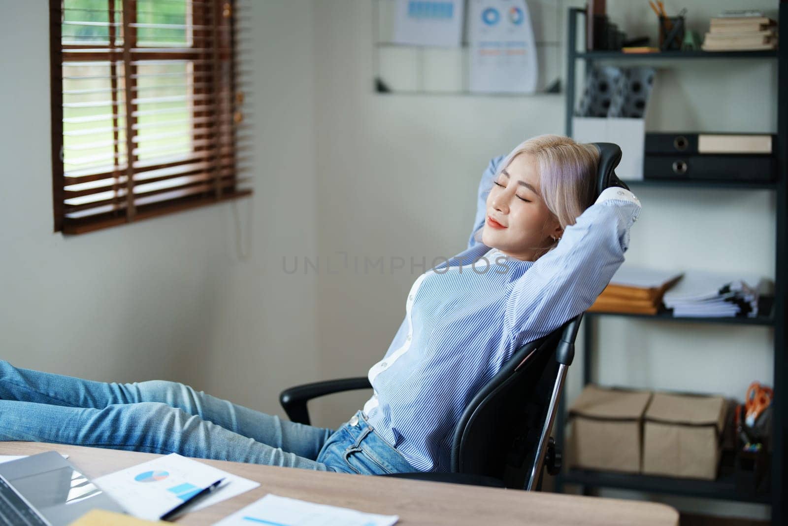 Portrait of a woman business owner showing a happy smiling face as he has successfully invested her business using computers and financial budget documents at work.