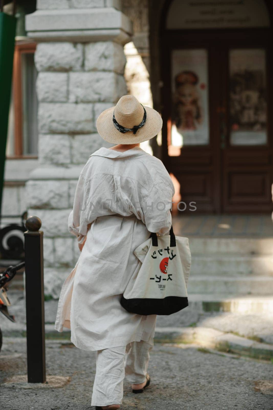 A woman in a hat in a white outfit with a bag walks around the Livadia Palace.