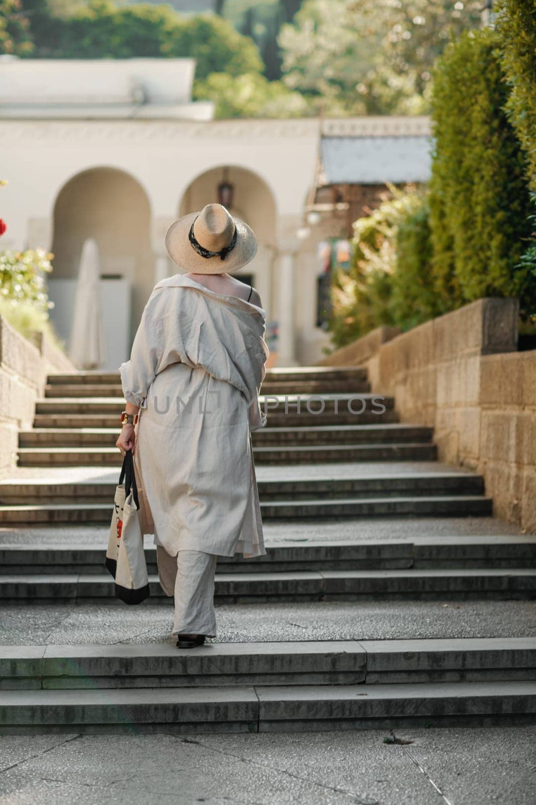 Woman on the stairs in the park. A middle-aged lady in a hat in a white outfit with a bag walks around the Livadia Palace.