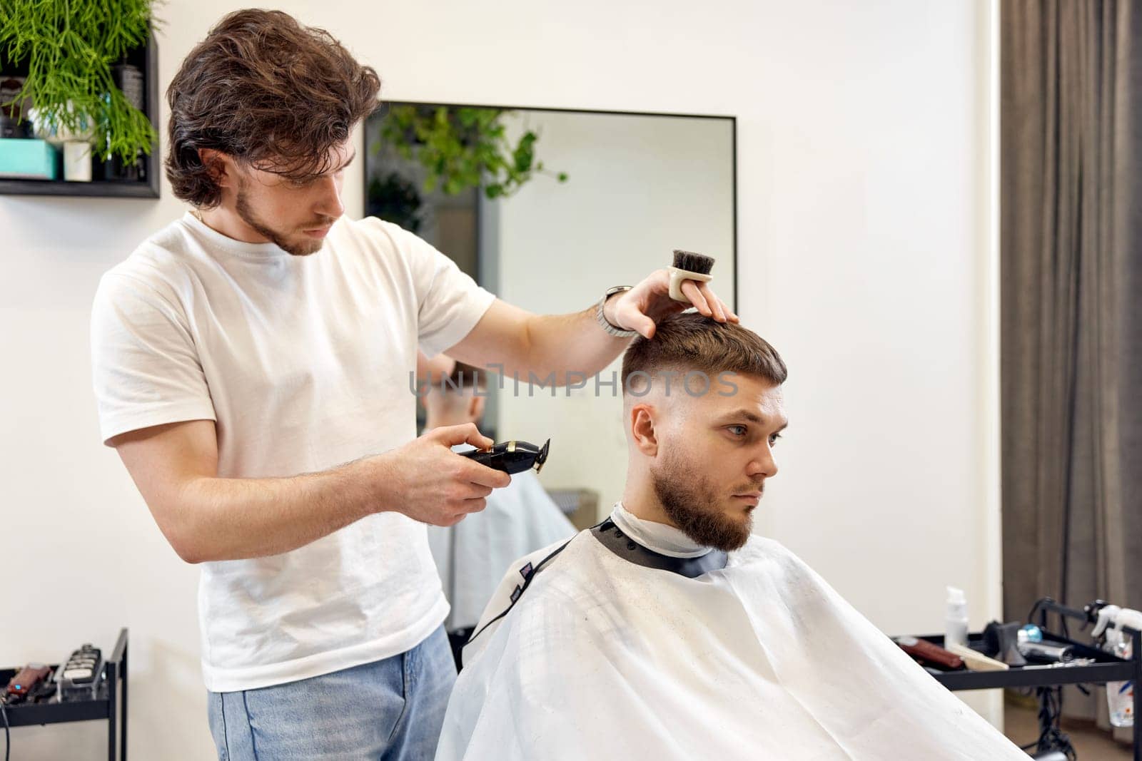 Barber trim hair with clipper on handsome bearded man in barber shop.