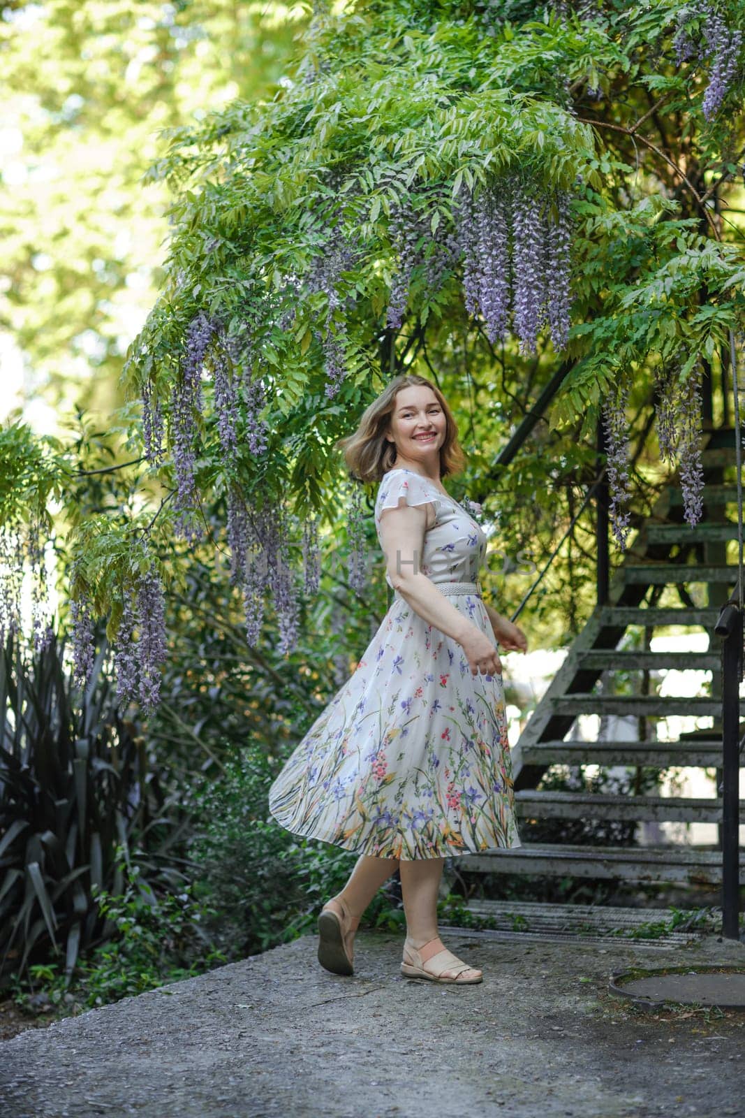 Wisteria woman. Thoughtful happy mature woman surrounded by chinese wisteria by Matiunina