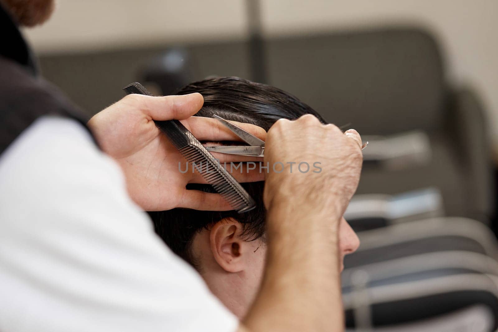 close-up, professional hairstylist does haircut for caucasian client man at barber shop.