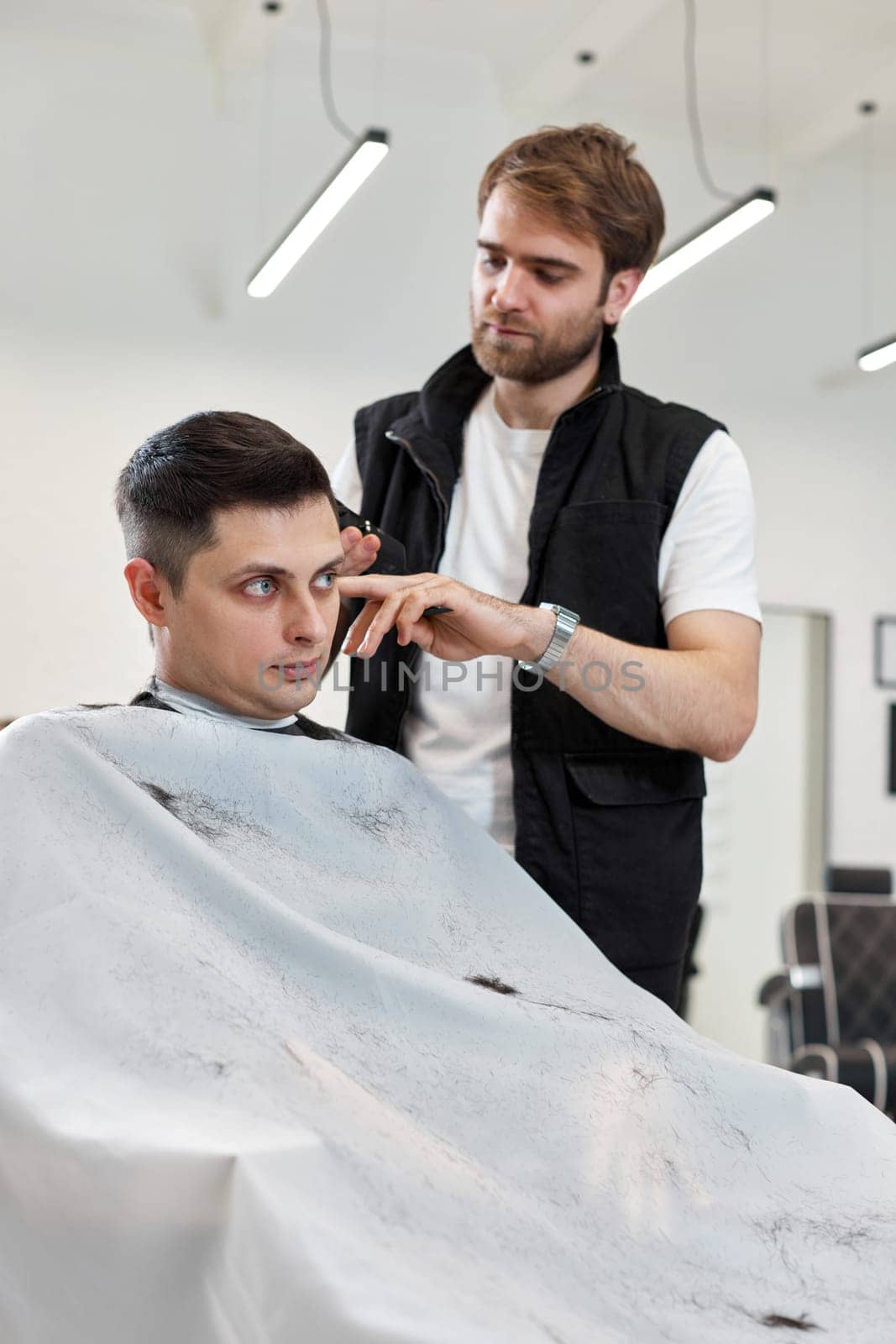 Barber shaving handsome caucasian man in barber shop.