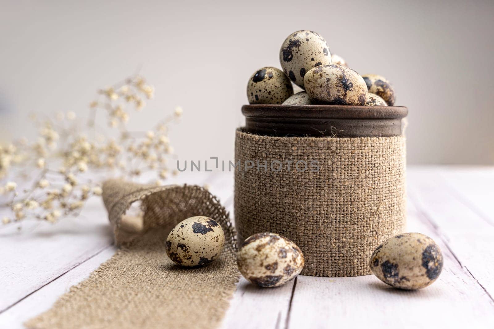 Fresh quail eggs in a clay mug on the table. Bright spring festive background and a branch of gypsophila. Close-up. Healthy eating. Easter.