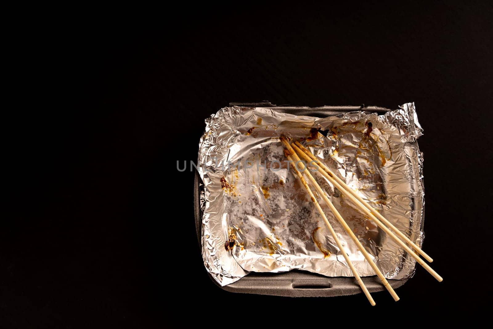 An empty plastic container for the delivery of a set of sushi. Chopsticks and an empty thermobox with foil inside for a set of sushi on a dark background. lunch. View from above. Flat lay. Copy space