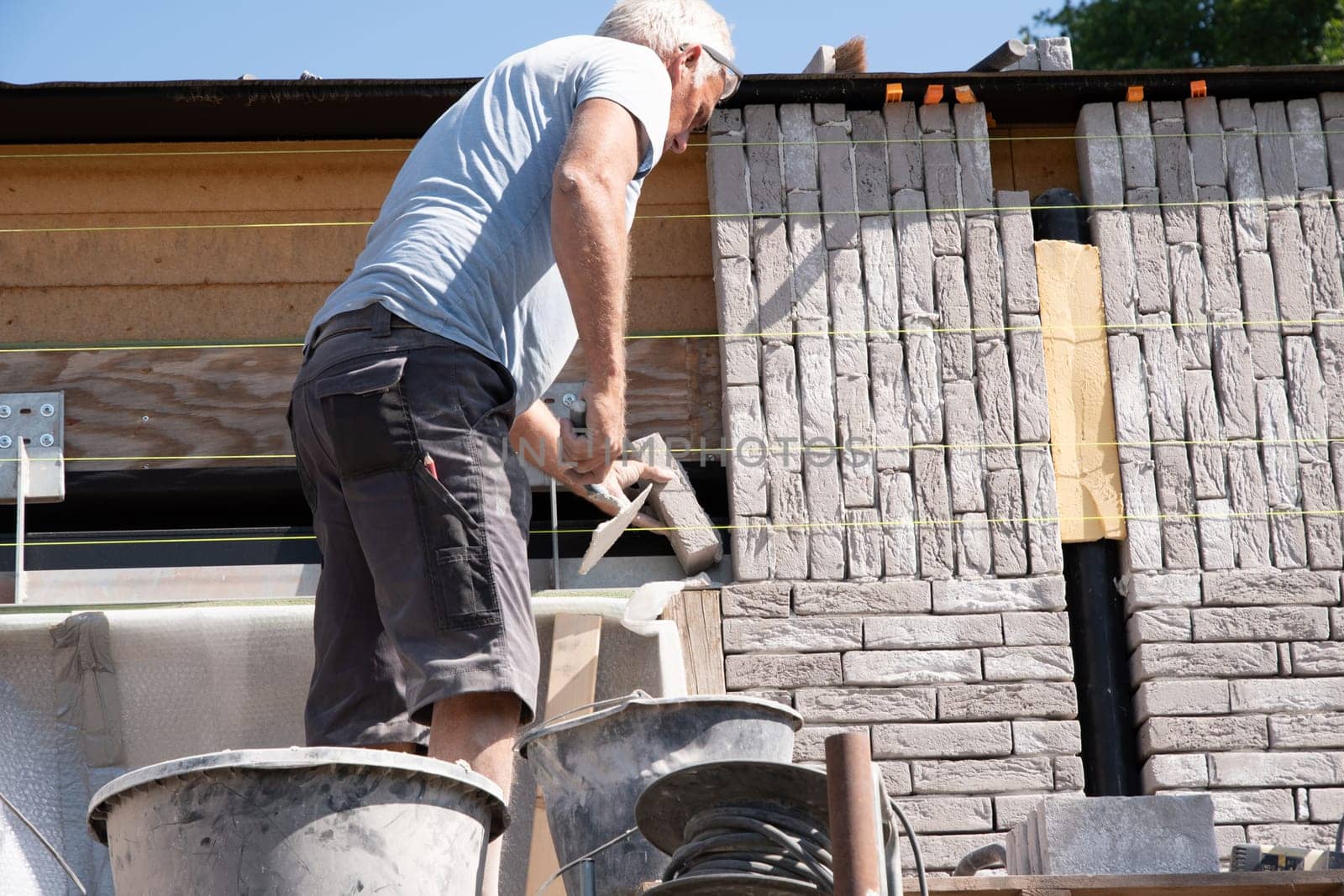 the bricklayer makes the facade of the house from gray bricks with cement and plaster at the construction site. High quality photo