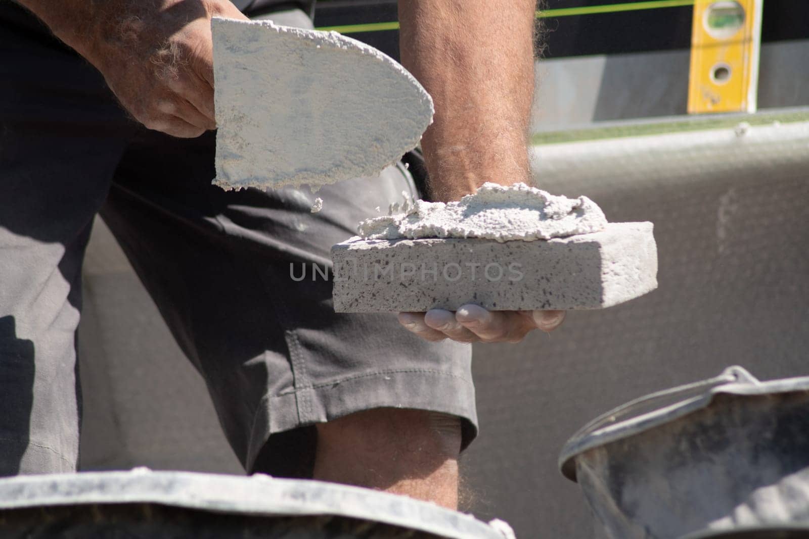 close up of the hands of a bricklayer applying cement mortar to a brick to stick it into the masonry for building a house, High quality photo