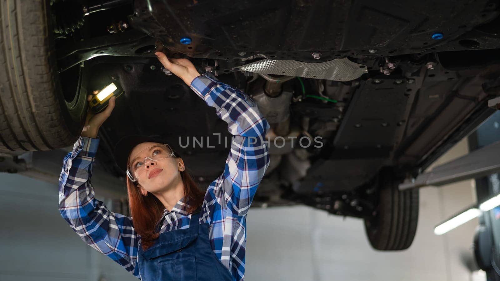 A female mechanic inspects a lifted car. A girl at a man's work