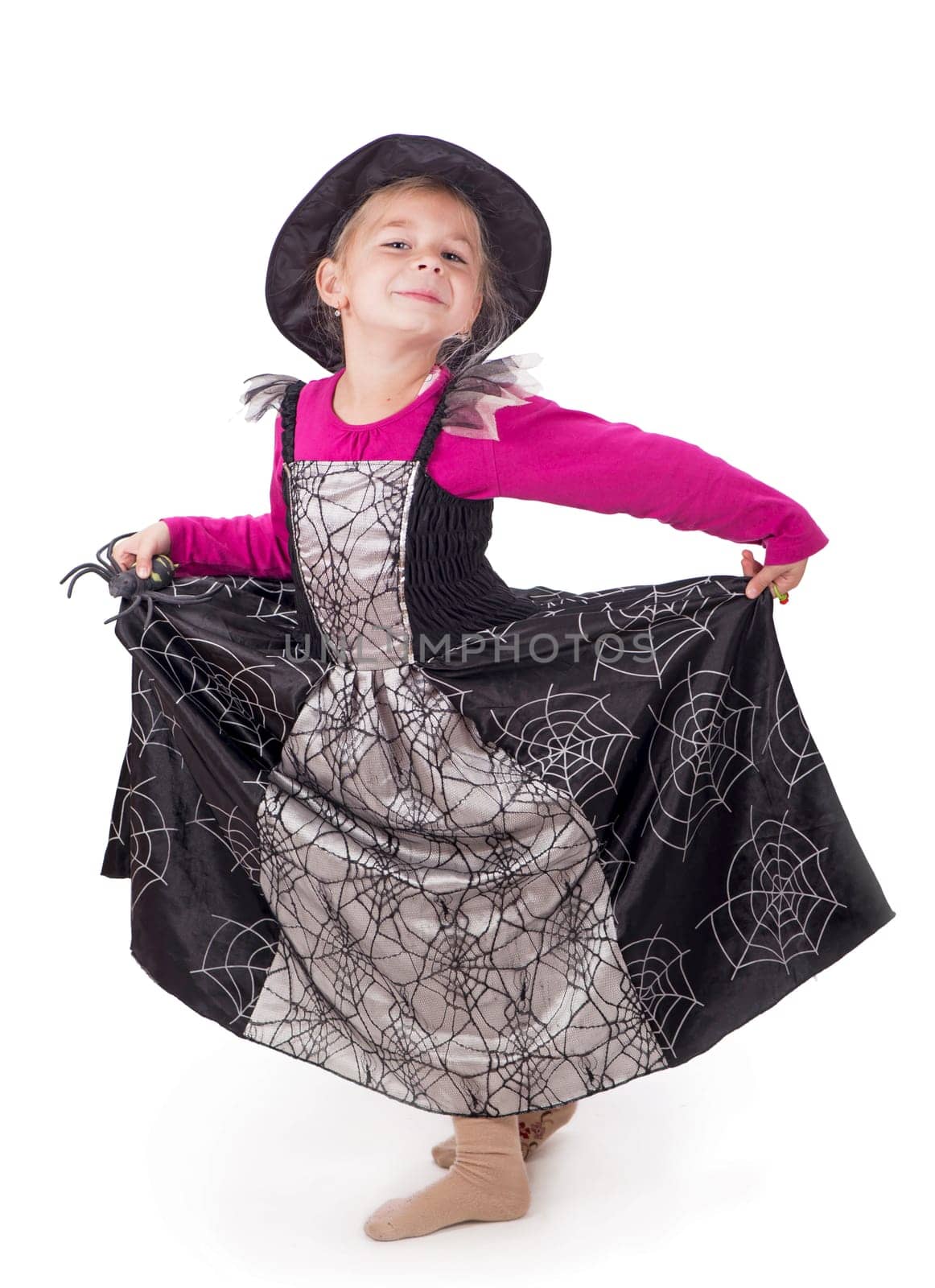 Little witch sorceress goes to a masquerade girl in a halloween costume holds a black toy spider in her hands on a white background by aprilphoto