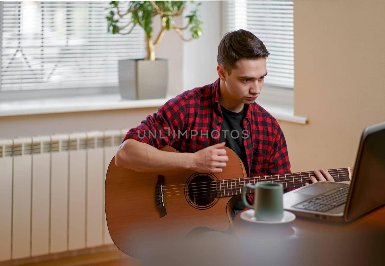 Young man learning to play guitar online by aprilphoto