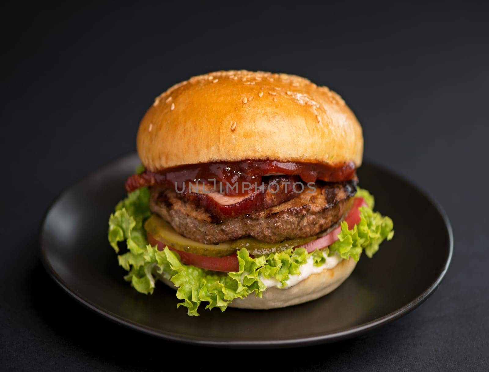 Big tasty burger with beef patty, lettuce, bacon and pickle on black background by aprilphoto