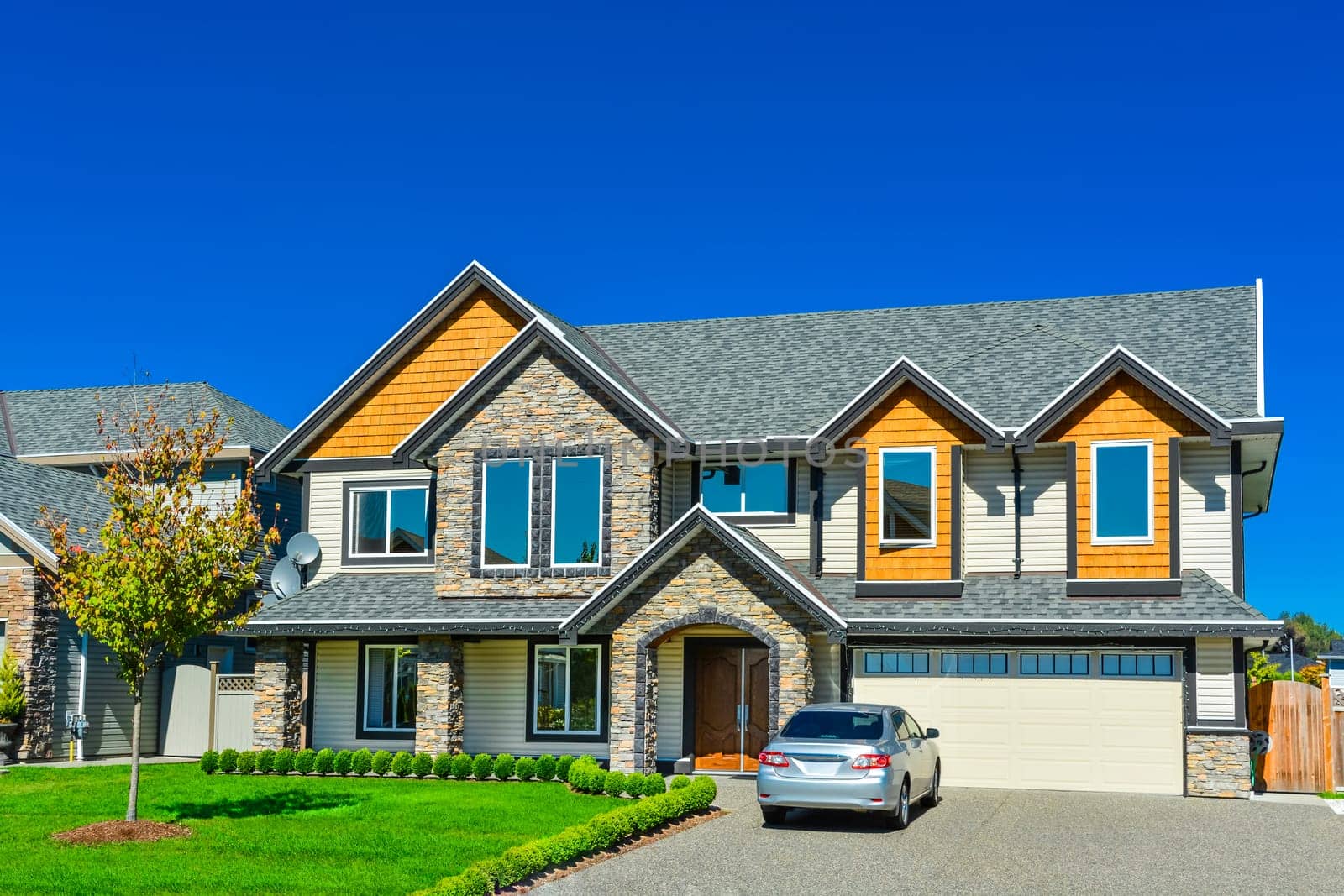 A perfect neigborhood. Luxury residential house with concrete driveway, wide garage door on blue sky background.