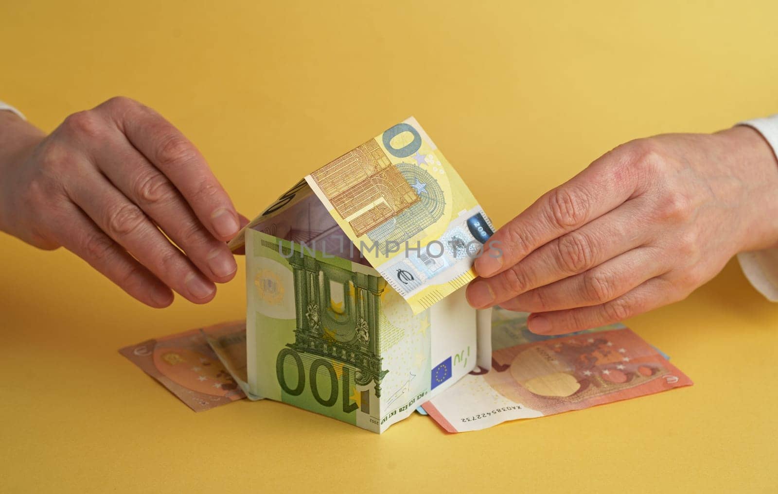 Businessman's hand holding house made of euro notes on table