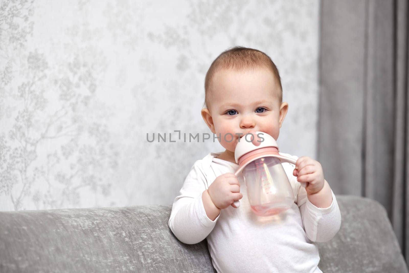 cute baby girl holding bottle and drinking water at home.