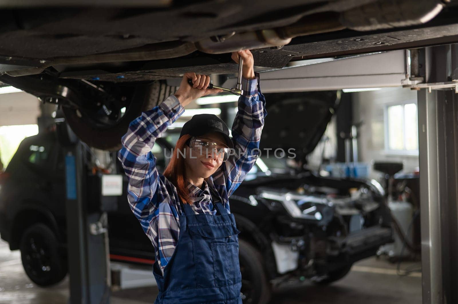 Female mechanic unscrew the nuts on the bottom of the car that is on the lift. A girl at a man's work