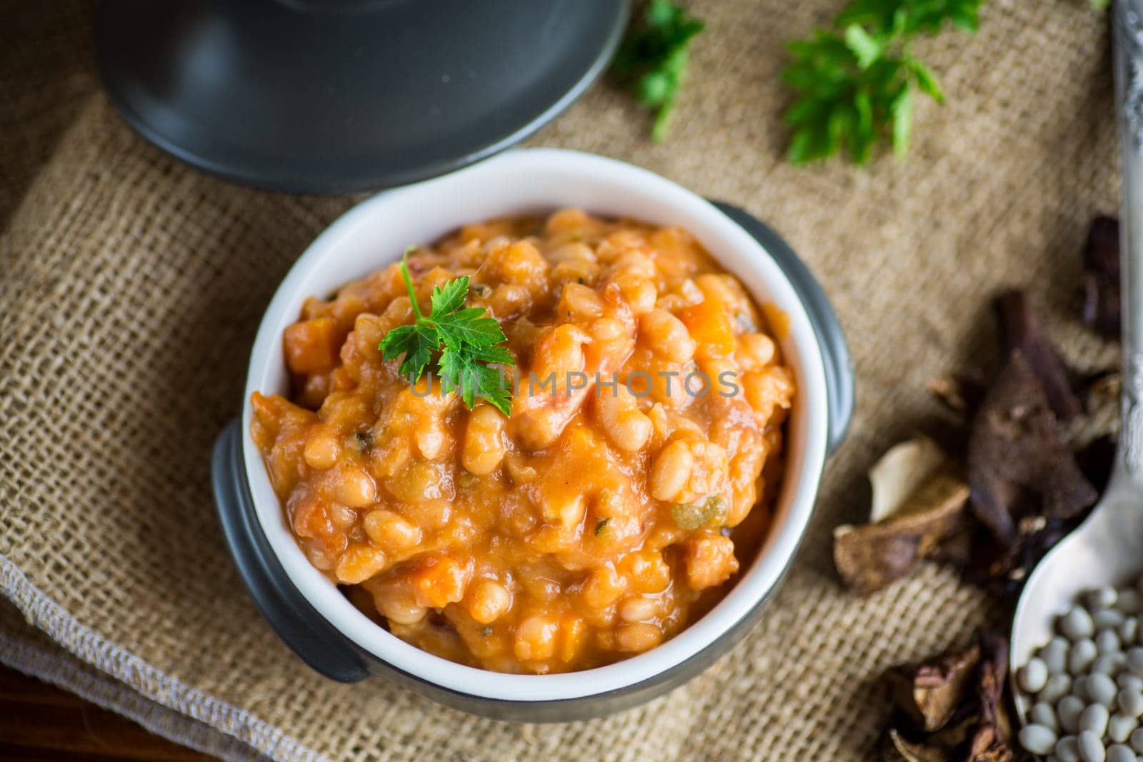beans stewed with vegetables, mushrooms and spices, in a bowl, on a wooden table.