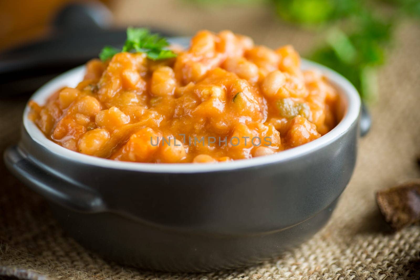 beans stewed with vegetables, mushrooms and spices, in a bowl, on a wooden table.