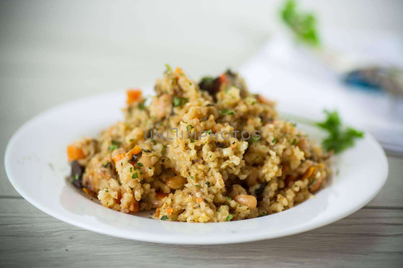 cooked bulgur with vegetables, carrots and dried mushrooms in a plate on a wooden table.