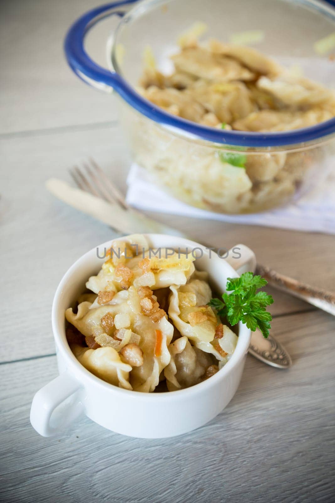 cooked dumplings with potatoes and fried onions, in a bowl on a wooden table.