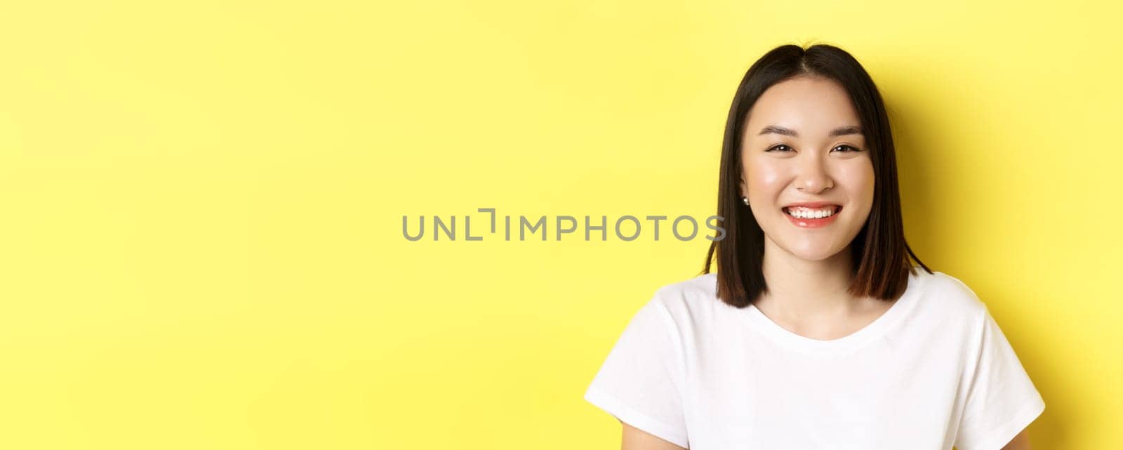 Beauty. Close up of smiling cute asian woman with perfect white smile teeth and glowing skin, standing over yellow background in t-shirt by Benzoix