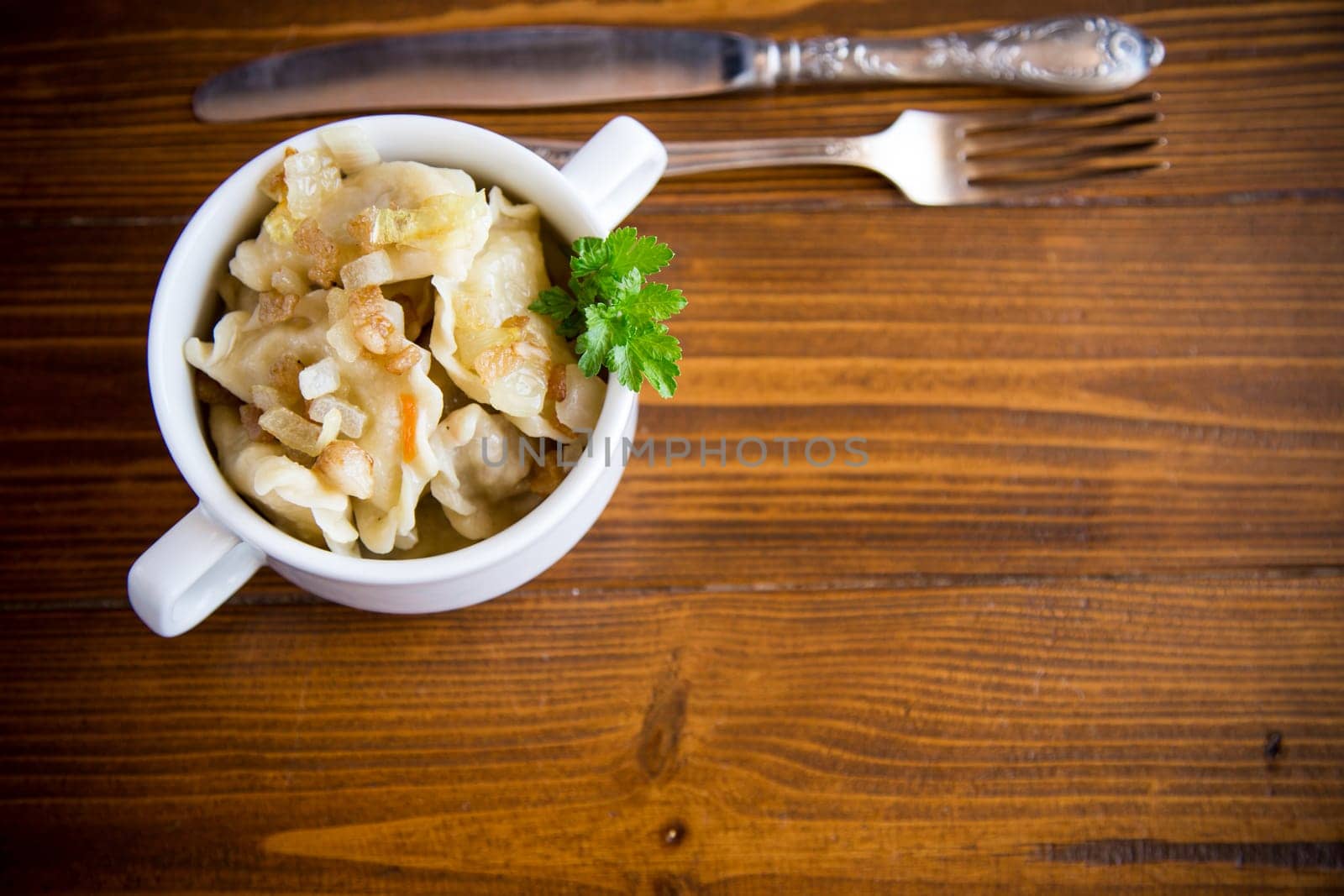 cooked dumplings with potatoes and fried onions, in a bowl on a wooden table.