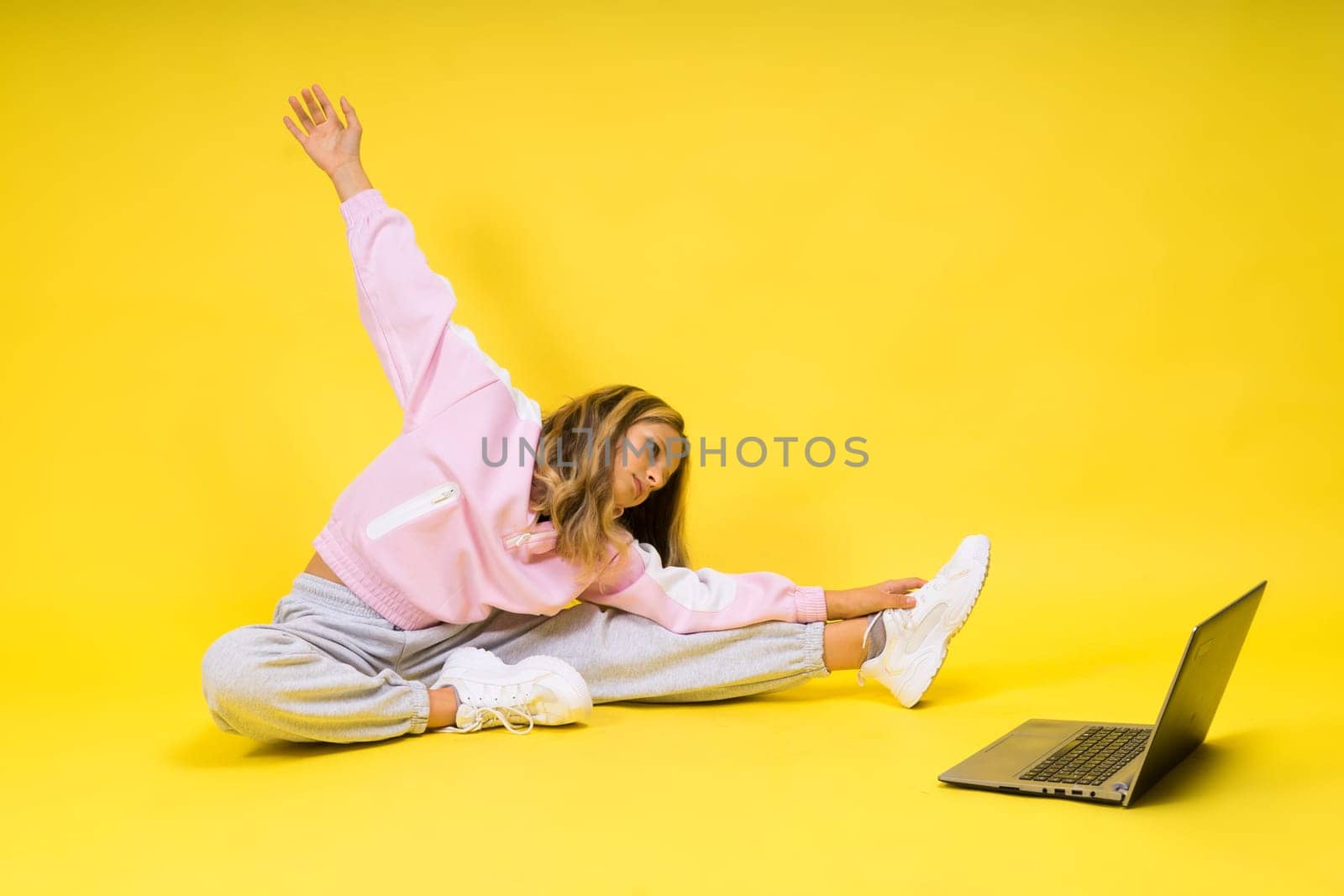 Fitness online. Girl doing stretching exercise on floor alone with laptop at studio by Zelenin