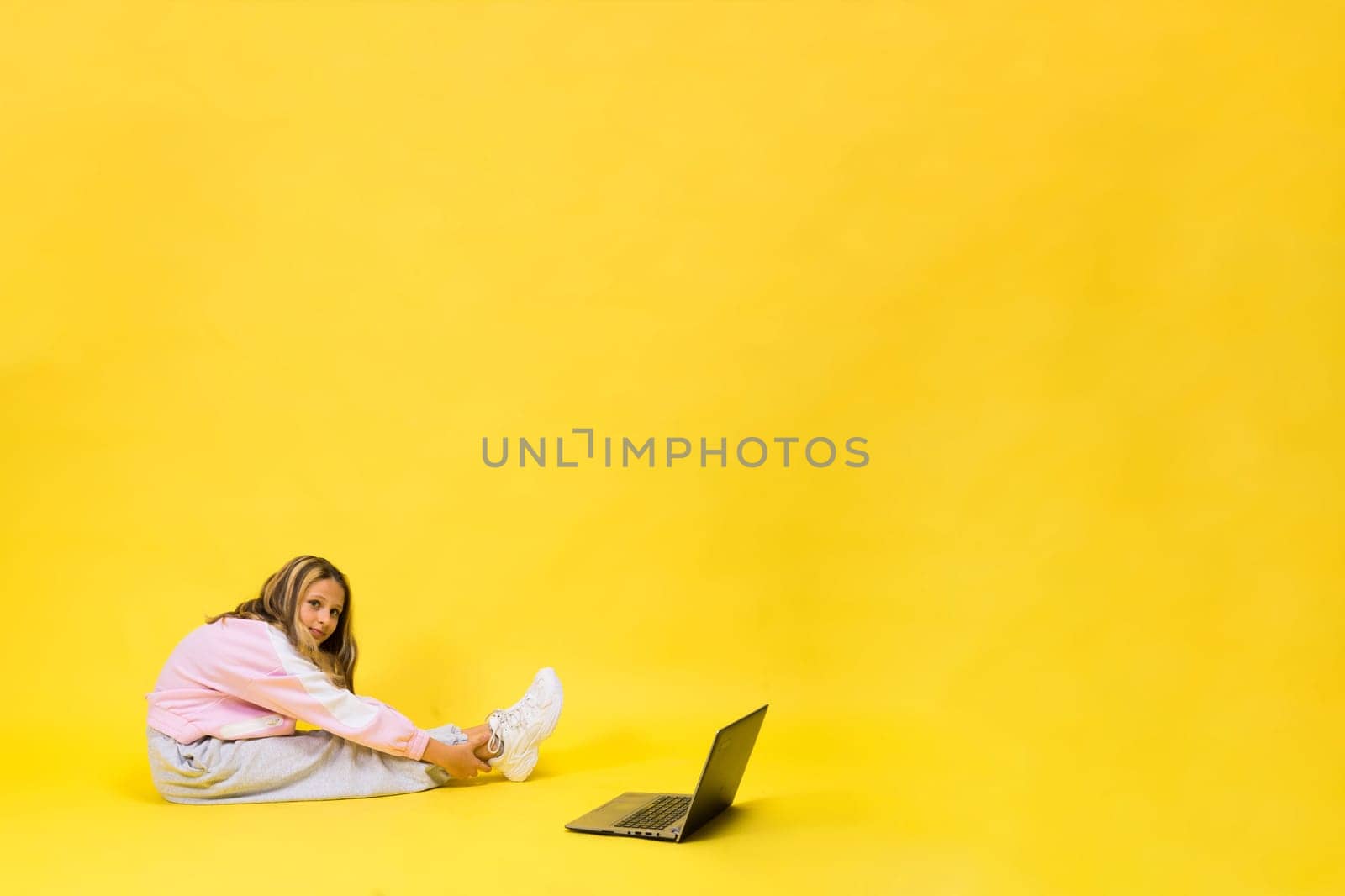 Fitness online. Girl doing stretching exercise on a floor alone with laptop at studio