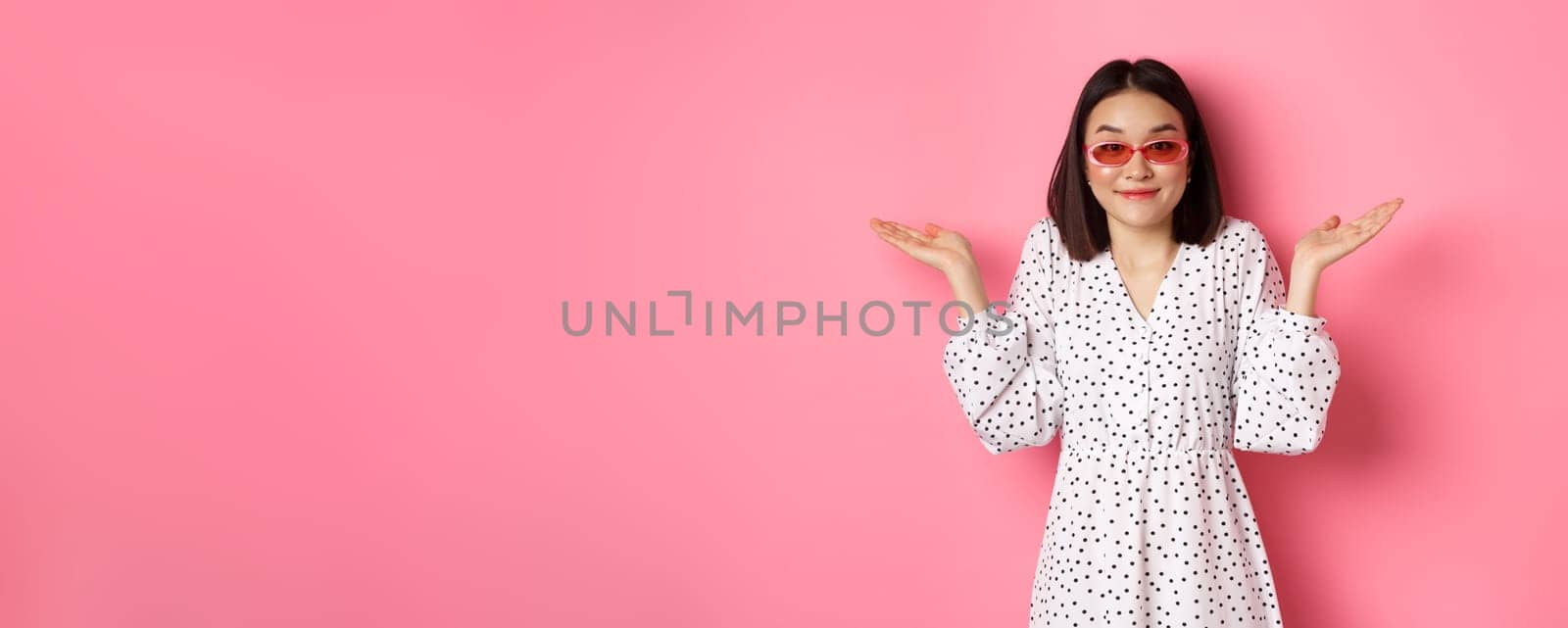 Cute asian woman tourist smiling at camera, shrugging clueless, dont know, wearing trendy sunglasses and white dress, standing against pink background by Benzoix