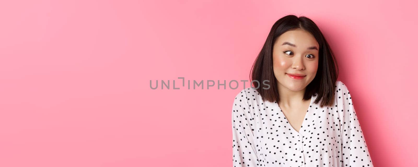 Beauty and lifestyle concept. Close-up of funny and cute asian woman squinting eyes and smiling, fool around at camera, standing over pink background by Benzoix