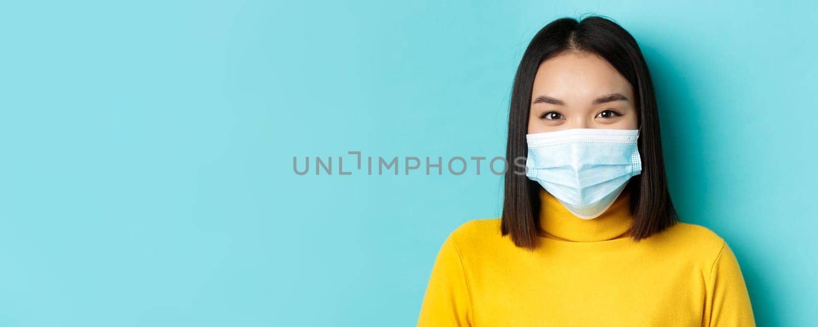 Covid-19, social distancing and pandemic concept. Close up of young asian woman with short dark hair, wearing medical mask and smiling with eyes, looking hopeful at camera.