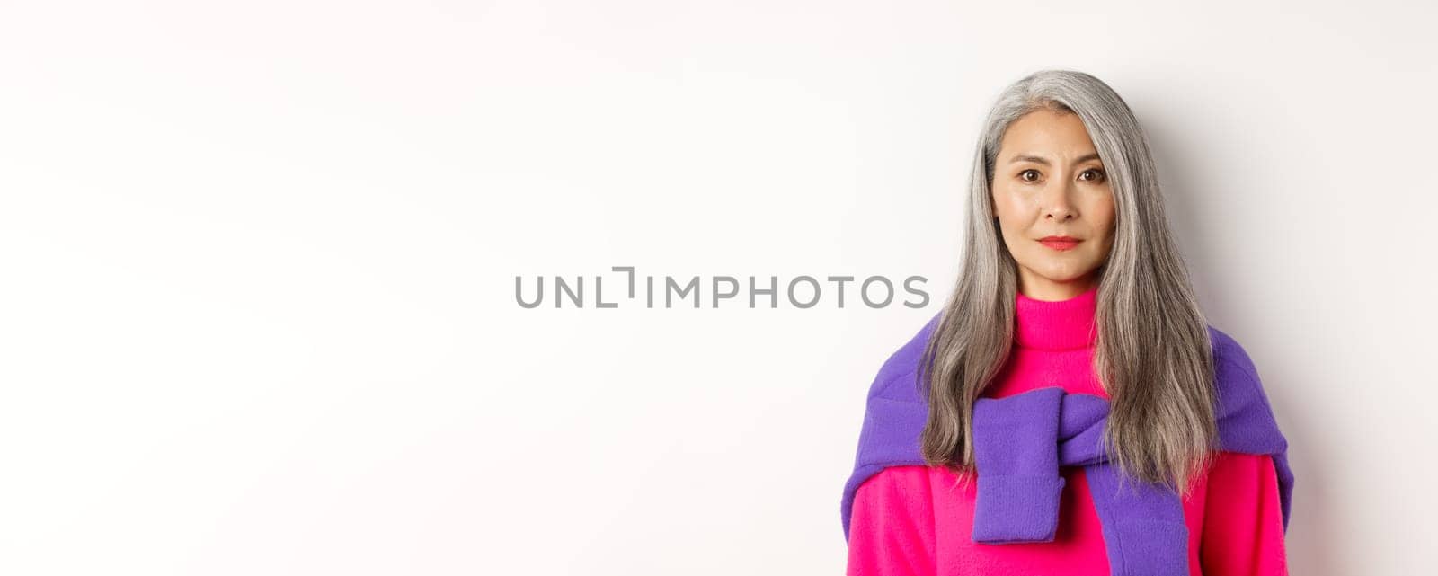 Close-up of stylish woman with grey hair and no wrinkles, smiling and looking at camera, standing in trendy outfit over white background by Benzoix