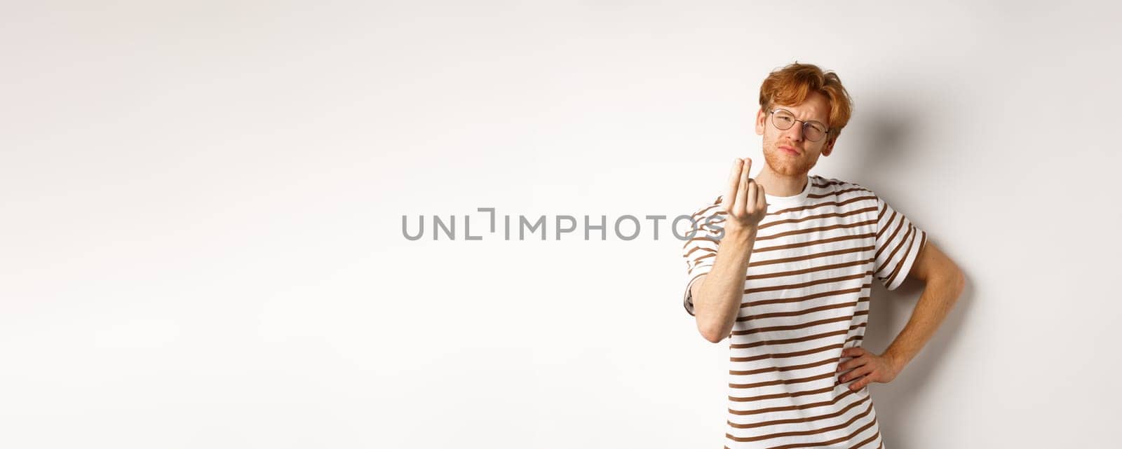 Image of satisfied young man with red hair and glasses showing chefs kiss gesture to praise something perfect, standing over white background.