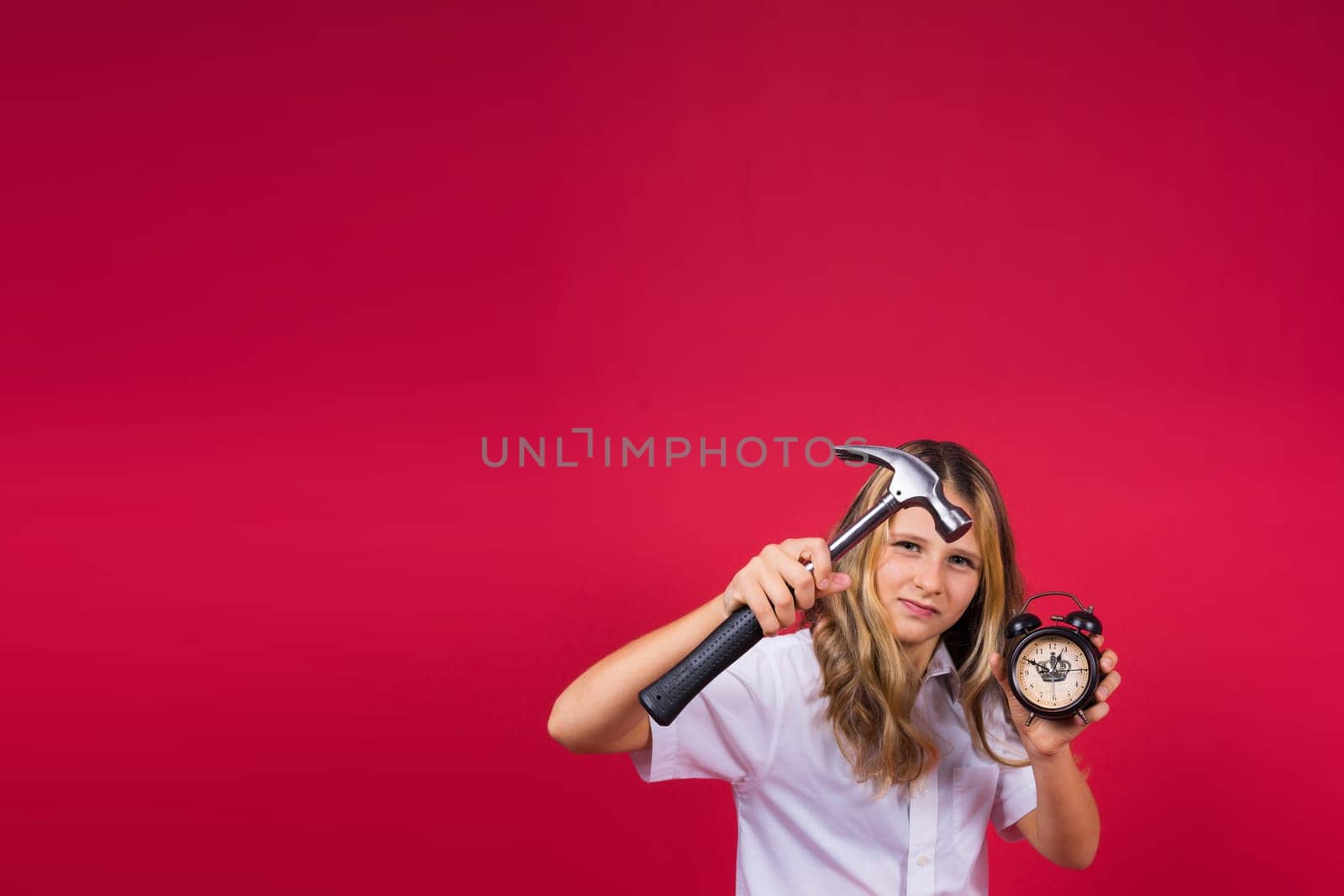 Young blonde girl holding an alarm clock and hammer smiling and laughing hard out loud.