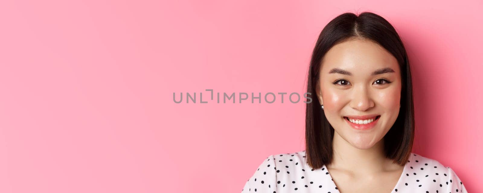 Beauty and lifestyle concept. Headshot of beautiful asian woman smiling, looking at camera happy and romantic, standing against pink background by Benzoix