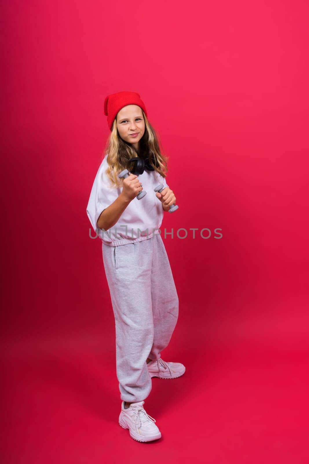 Kid girl doing fitness exercises with dumbbells on a red background