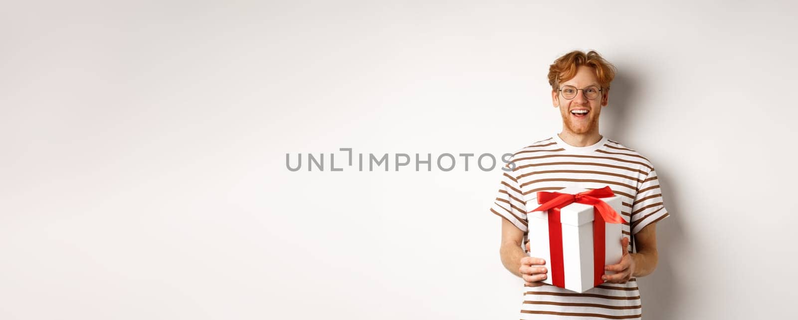 Valentines day and holidays concept. Cheerful young man holding gift box and smiling grateful, receiving presents, standing over white background.