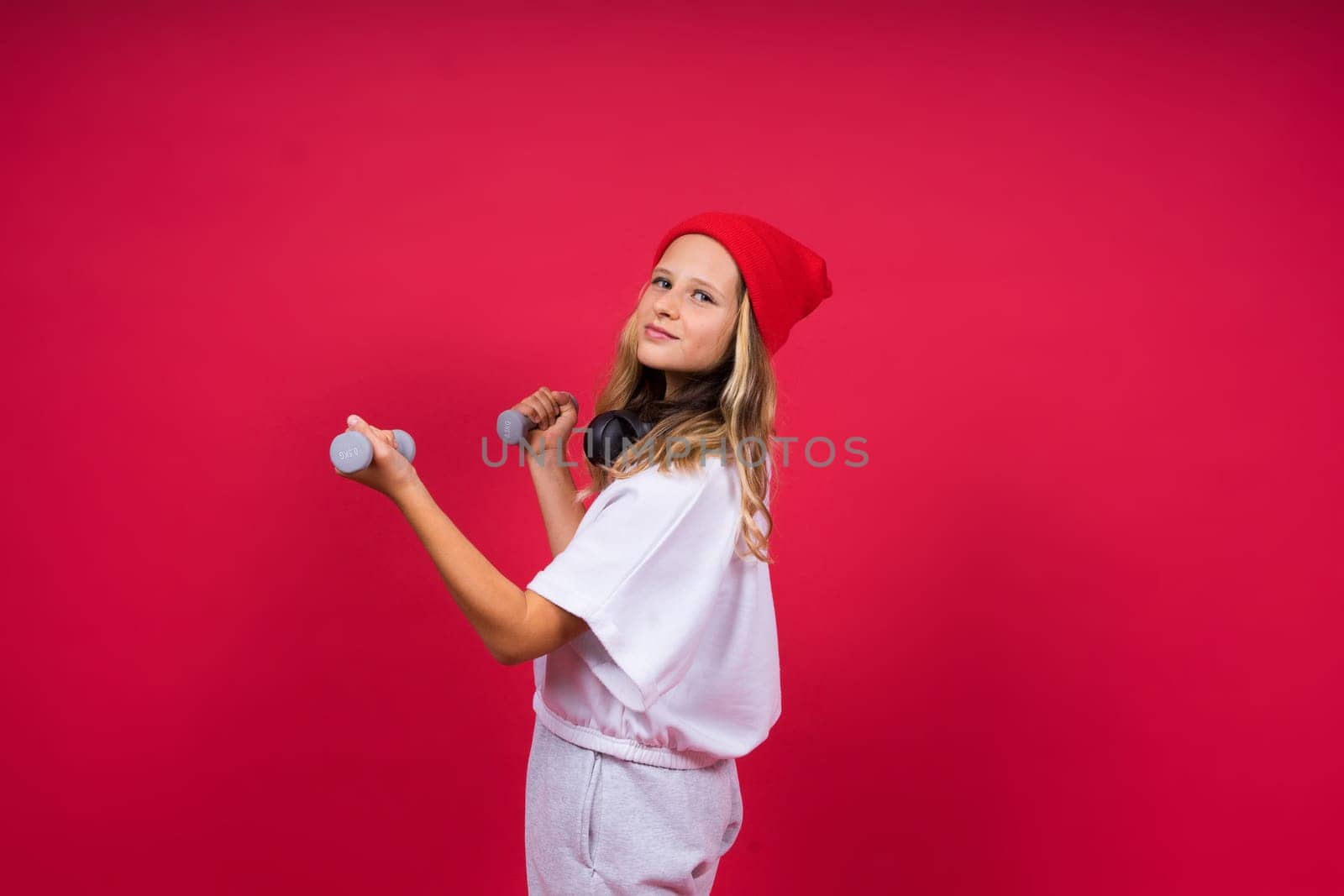 Kid girl doing fitness exercises with dumbbells on red background by Zelenin