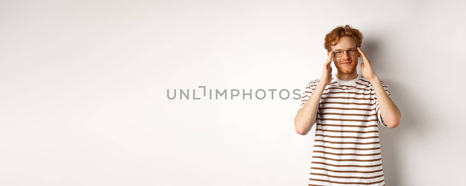 Handsome young man with hipster red hairstyle and glasses, smiling at camera, standing over white background.