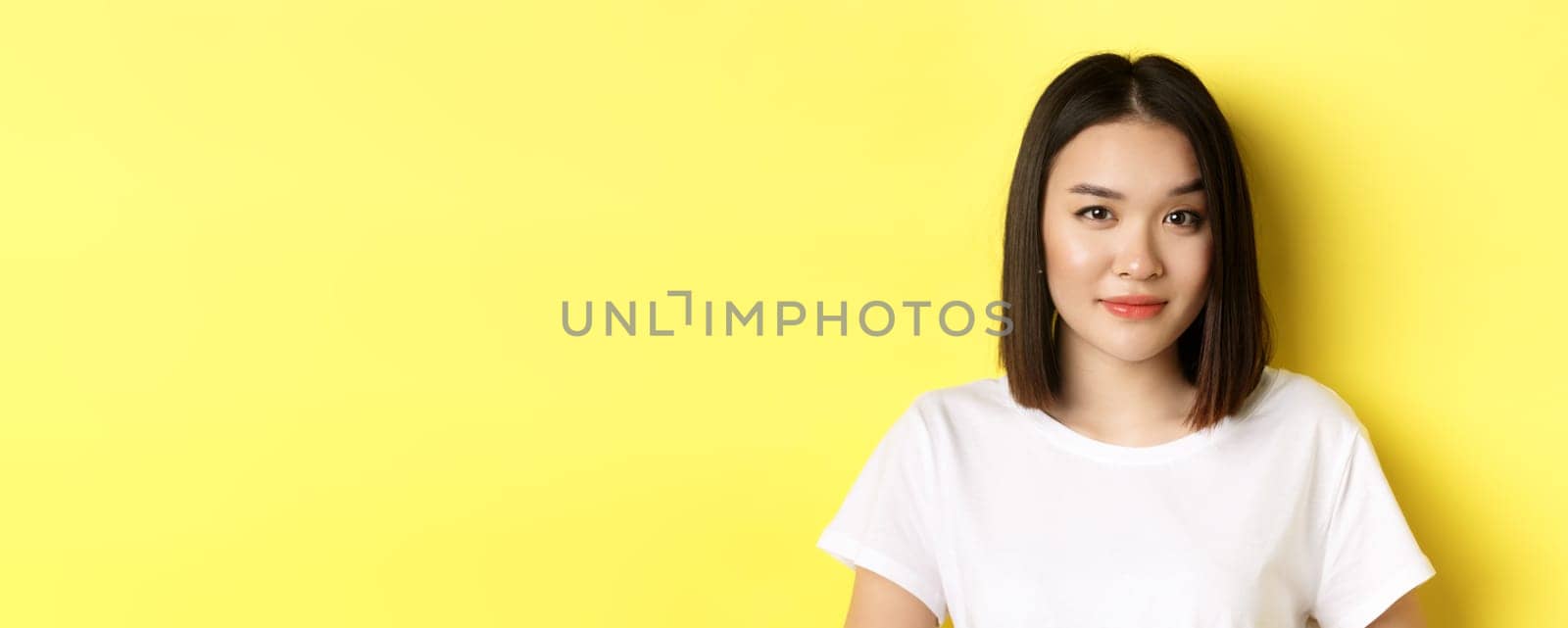 Close up of beautiful asian woman with casual makeup, raising eyebrow and looking intrigued at camera, standing curious over yellow background by Benzoix