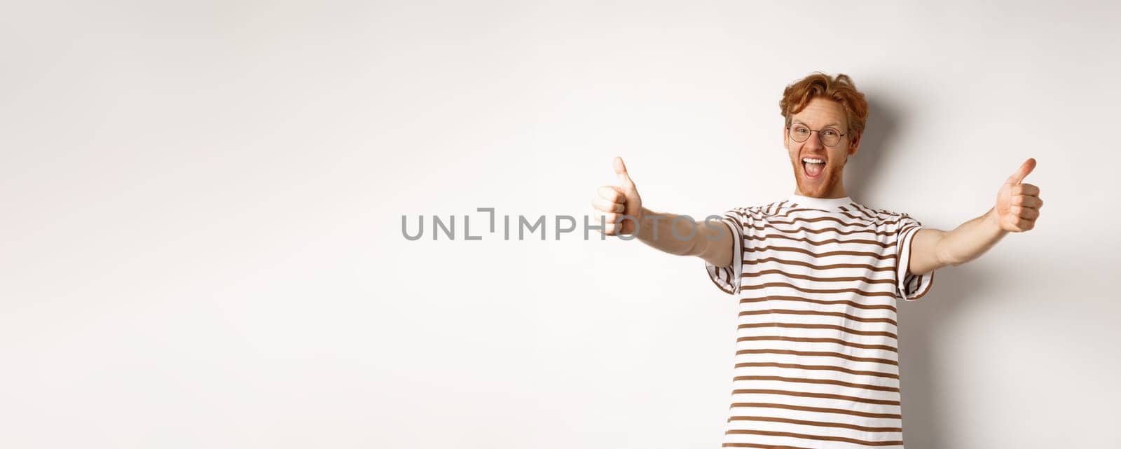 Happy redhead man scream yes and showing thumbs-up, approve and praise excellent company, standing over white background.