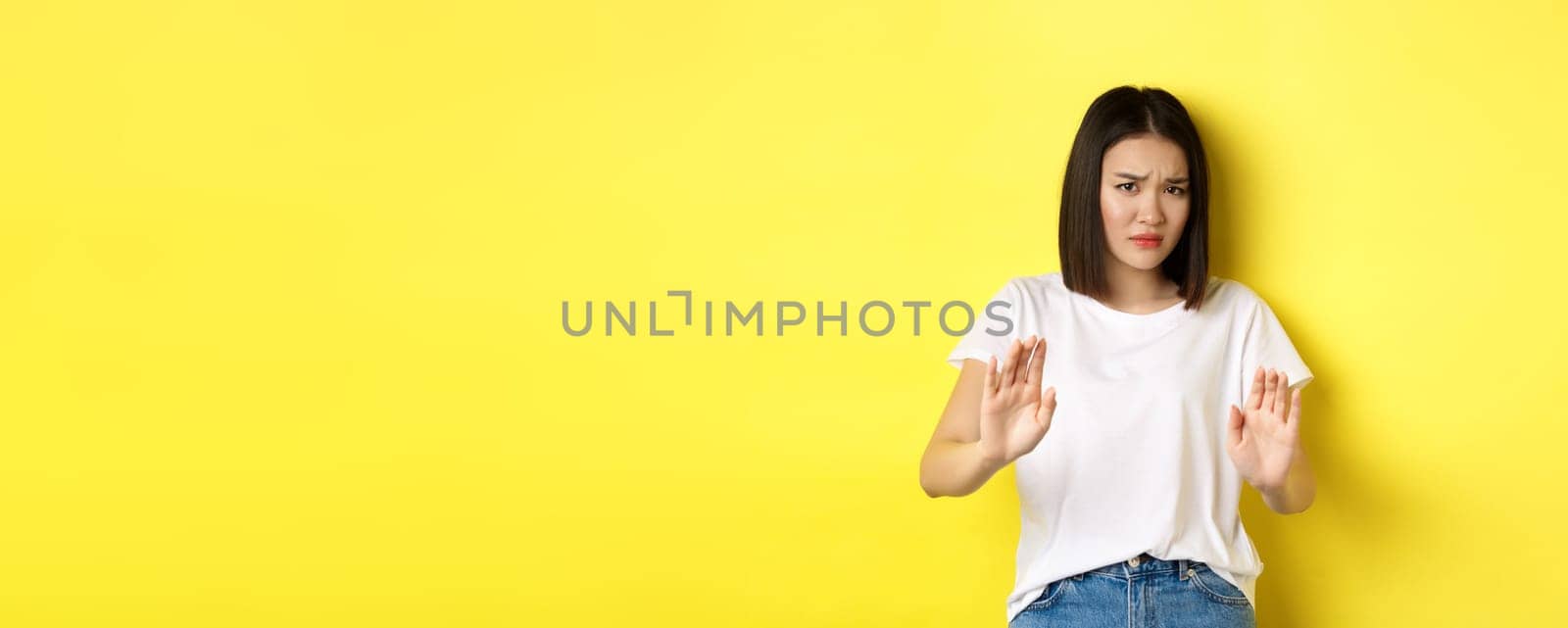 Please no. Asian woman, victim of assualt or domestic abuse, pleading with hands raised up in defense, frowning sad, begging stop, standing over yellow background by Benzoix